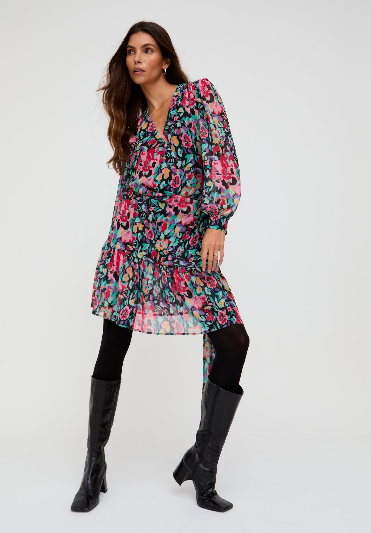 Woman wearing a floral dress with long sleeves and black knee-high boots on a white background