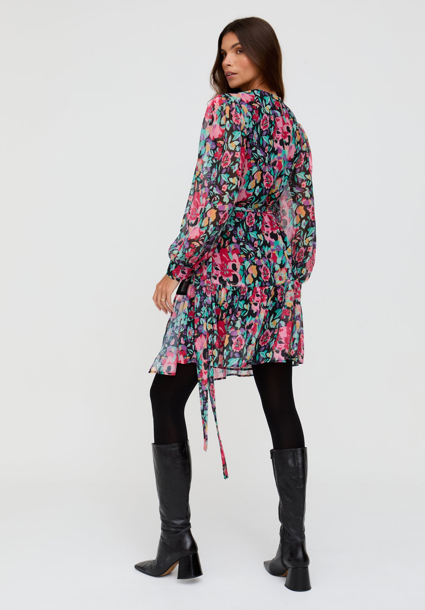 Woman wearing a colorful floral dress with black leggings and knee-high boots on a white background