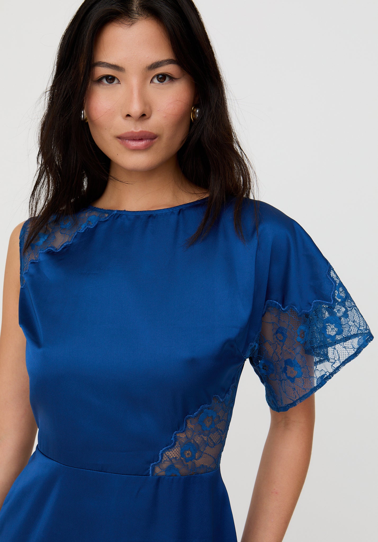 Woman wearing a blue dress with lace sleeves against a white background