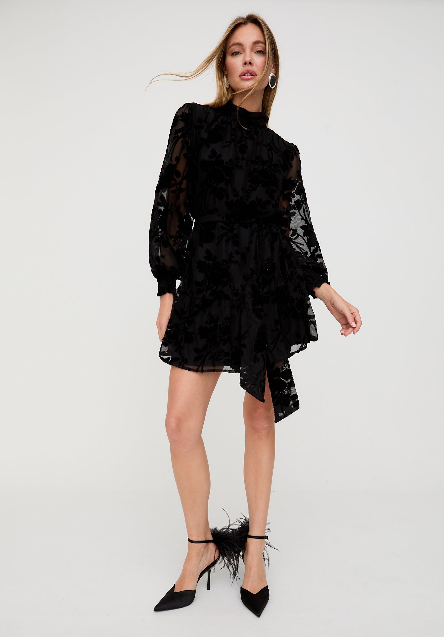 Woman wearing a black lace dress with sheer sleeves on a white background