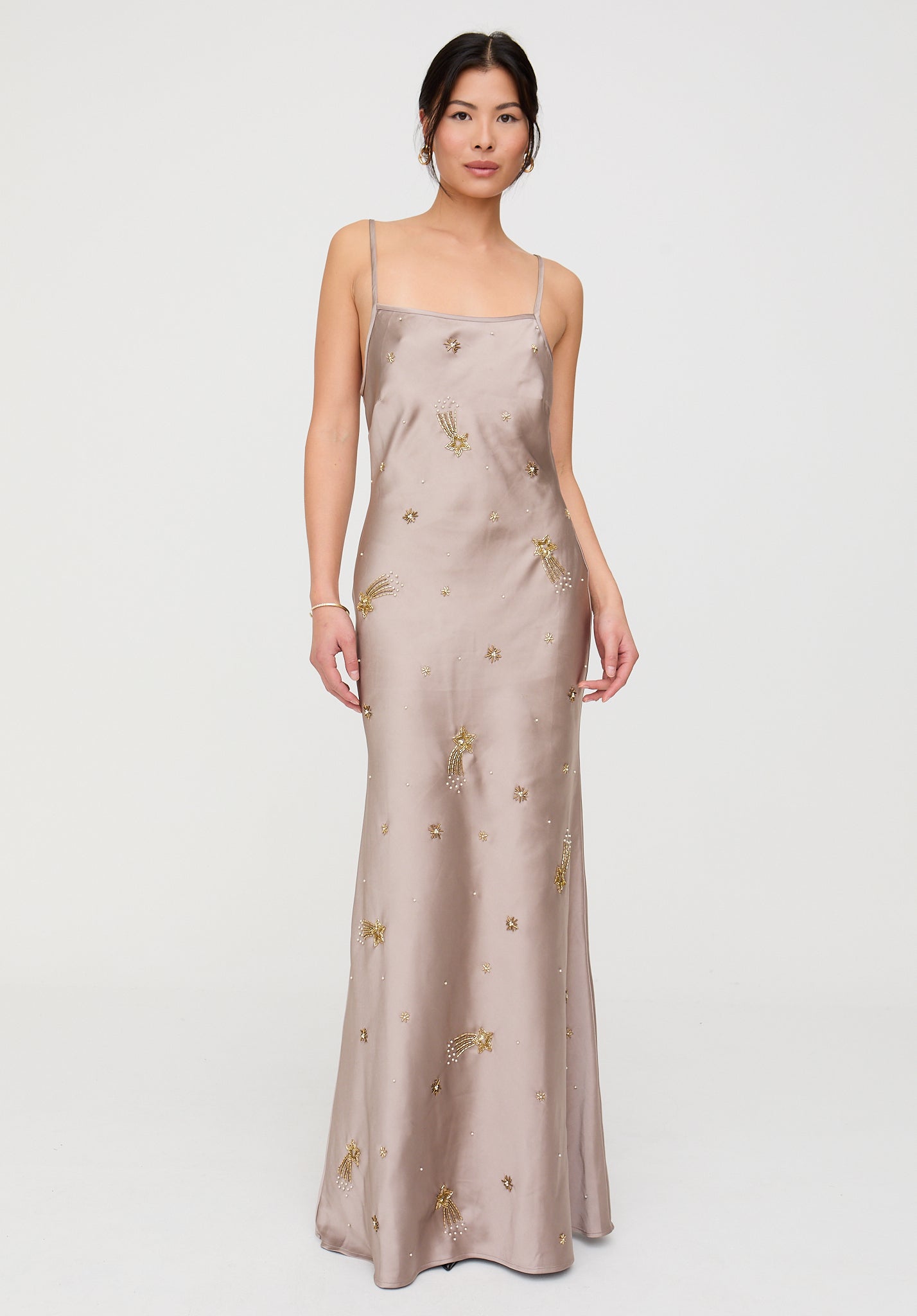 Woman wearing a long, light-colored dress with gold embellishments on a white background