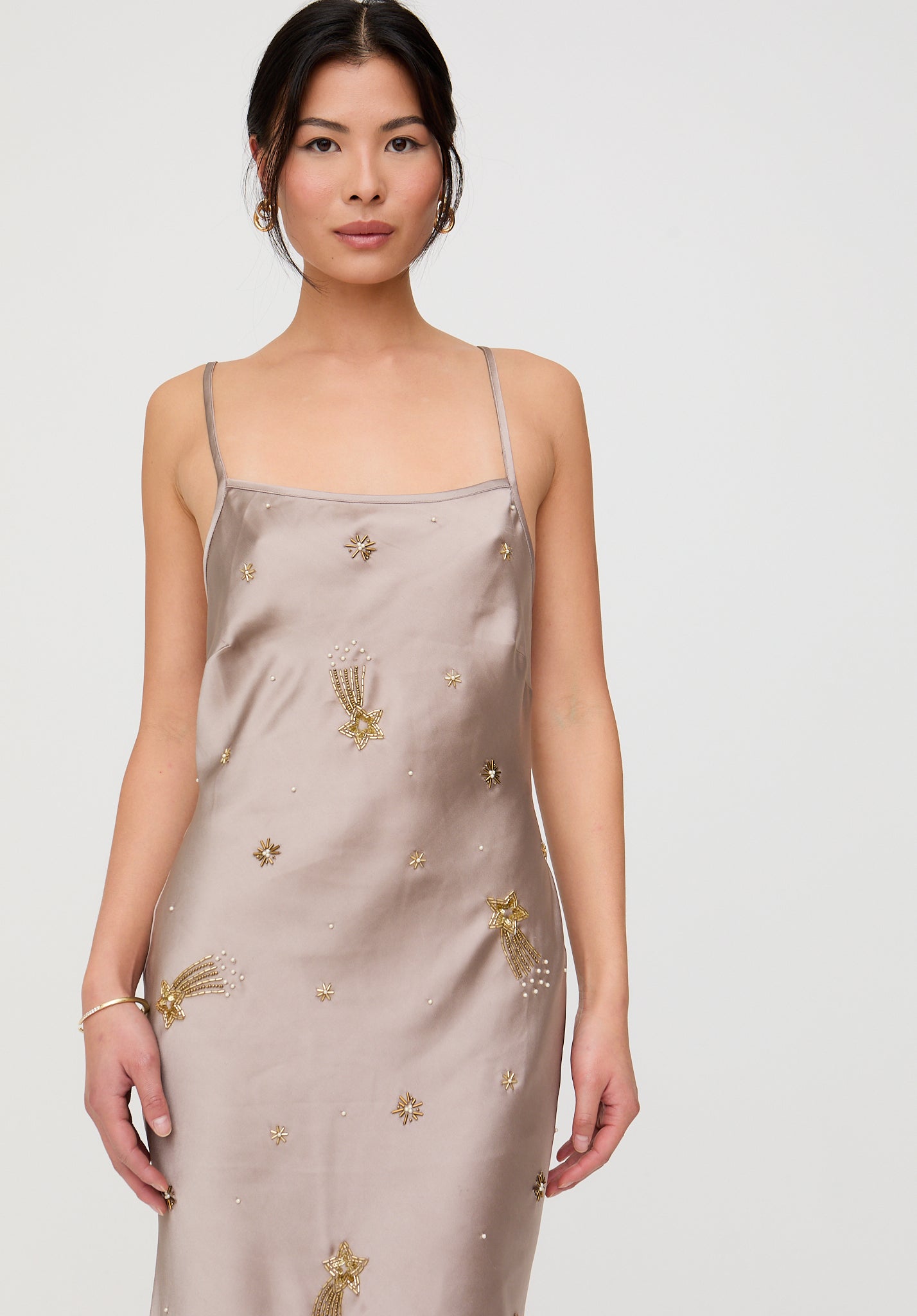 Woman wearing a beige slip dress with gold embroidery on a white background