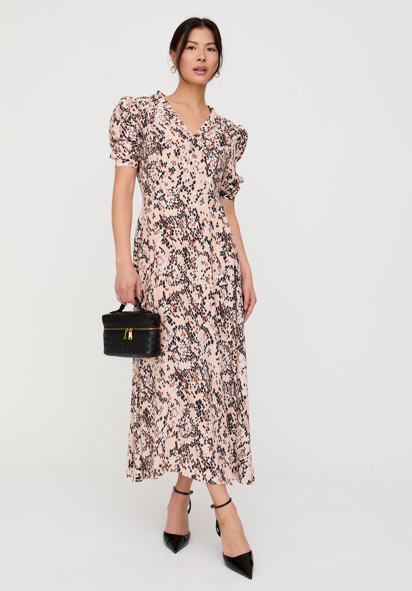 Woman wearing a floral dress holding a black handbag on a white background