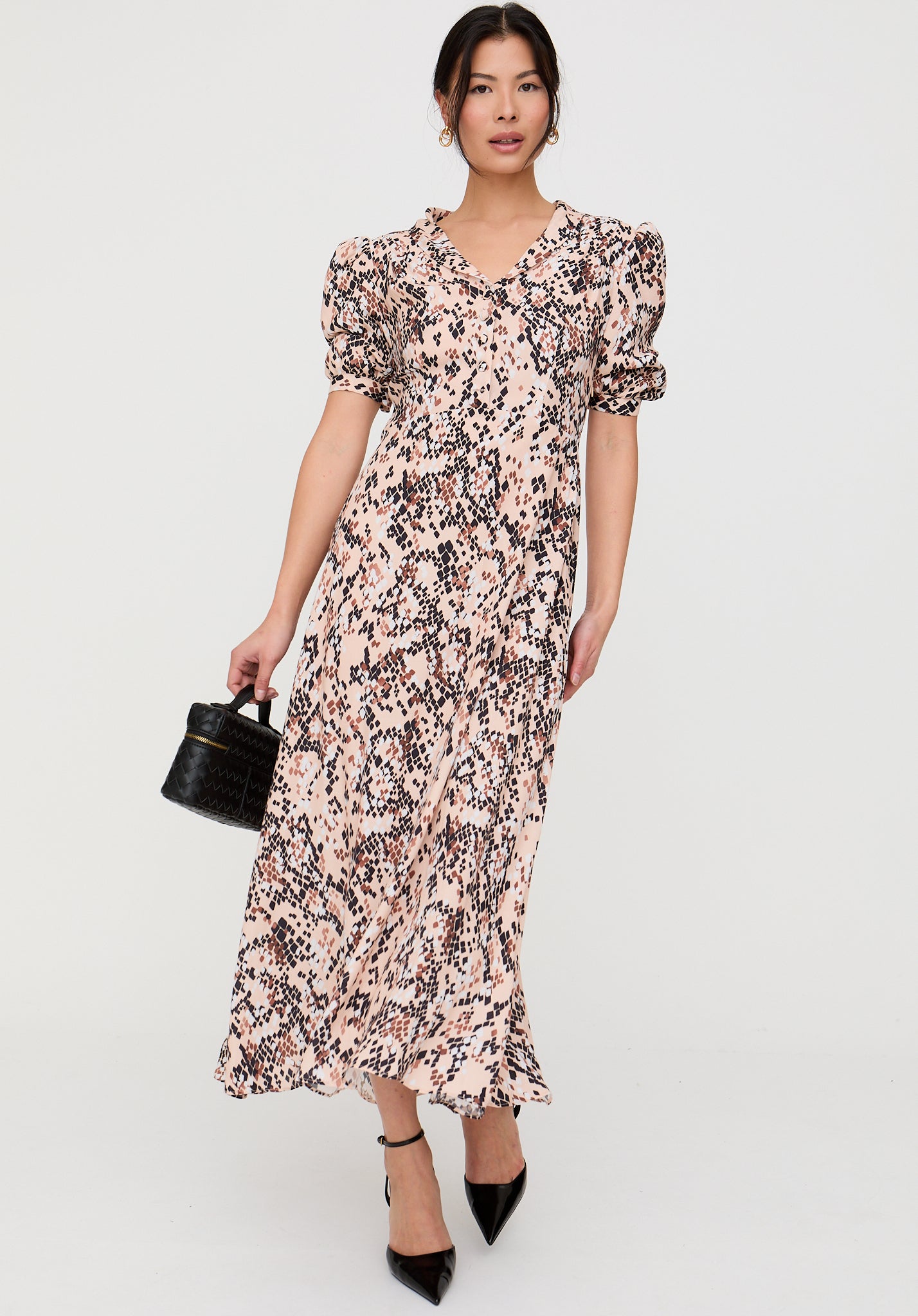 Woman wearing a floral dress holding a black handbag on a white background