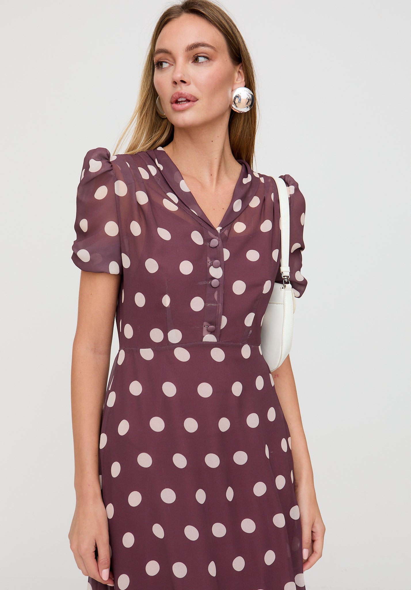 Woman wearing a purple dress with white polka dots on a plain background