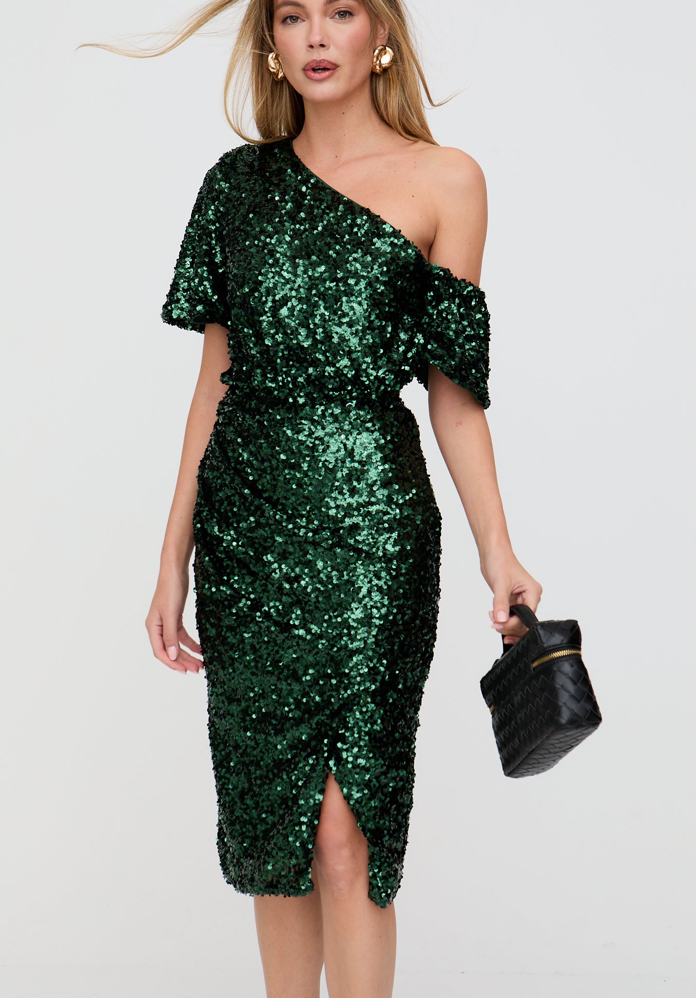 Woman wearing a green sequin dress holding a black handbag on a light gray background