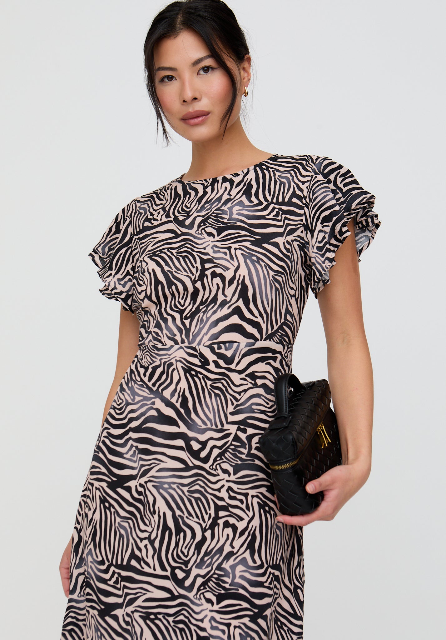 Woman wearing a zebra print dress holding a black clutch against a white background