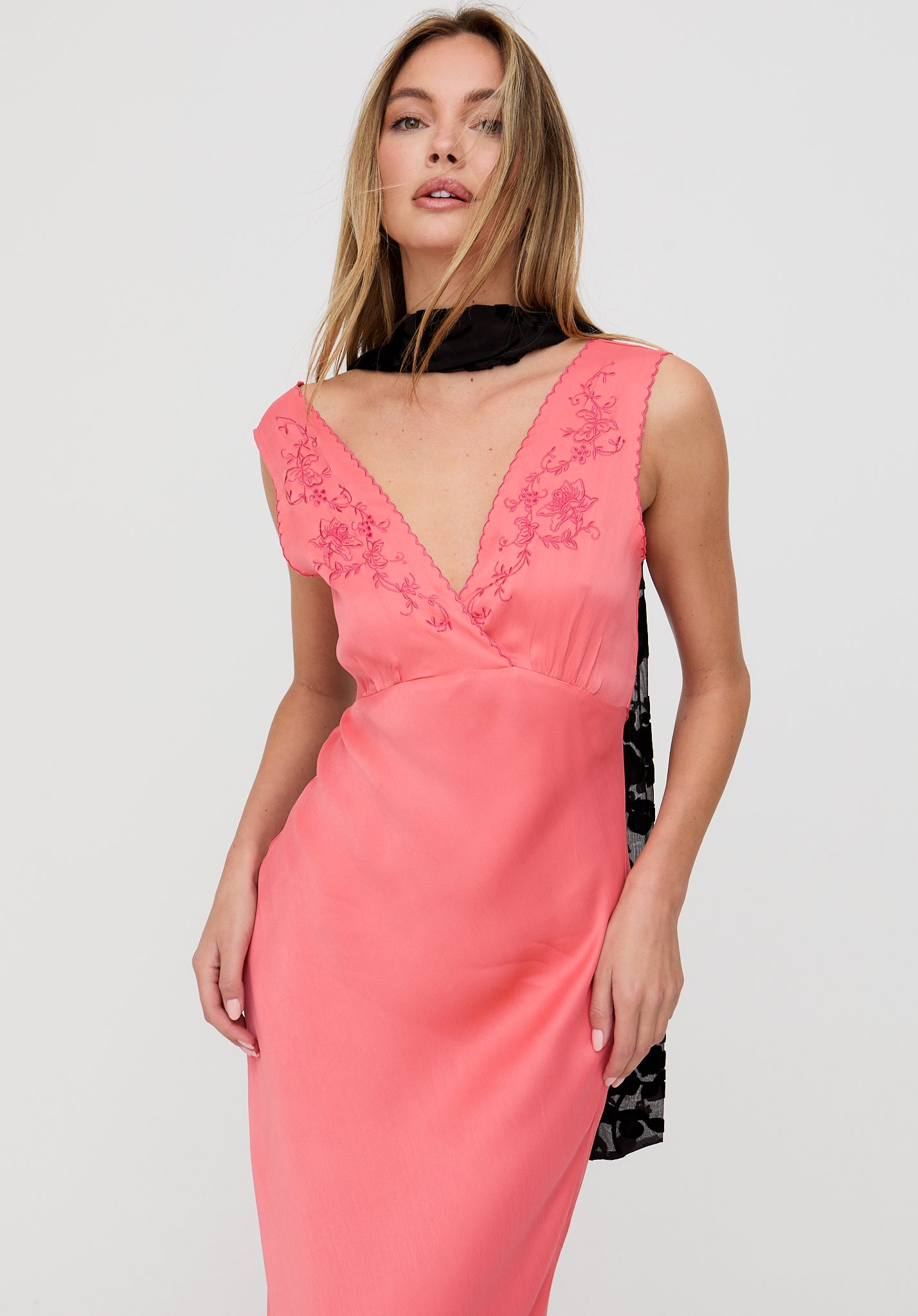 Woman wearing a pink dress with floral embroidery on a light gray background