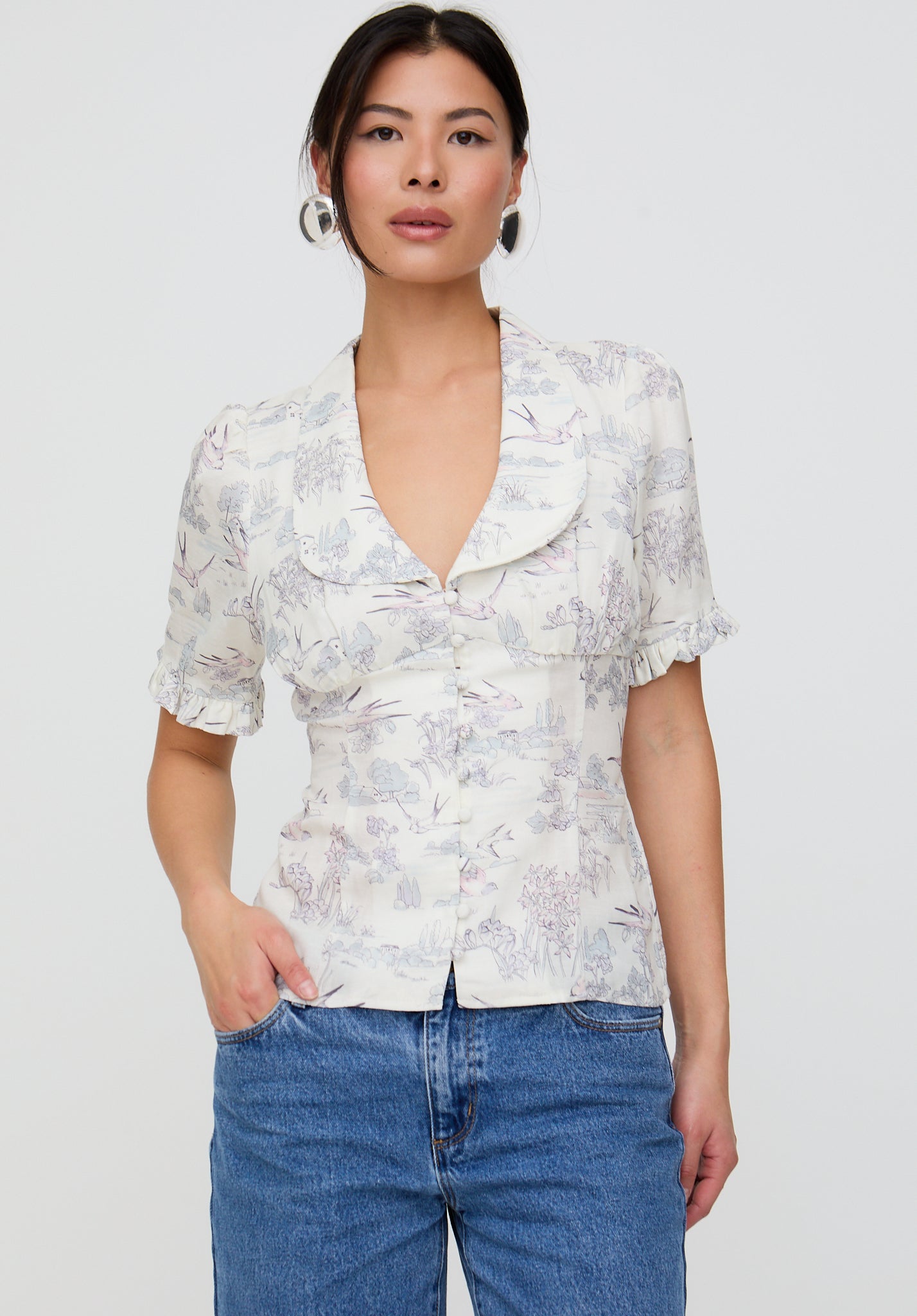 Woman wearing a floral blouse and blue jeans against a white background