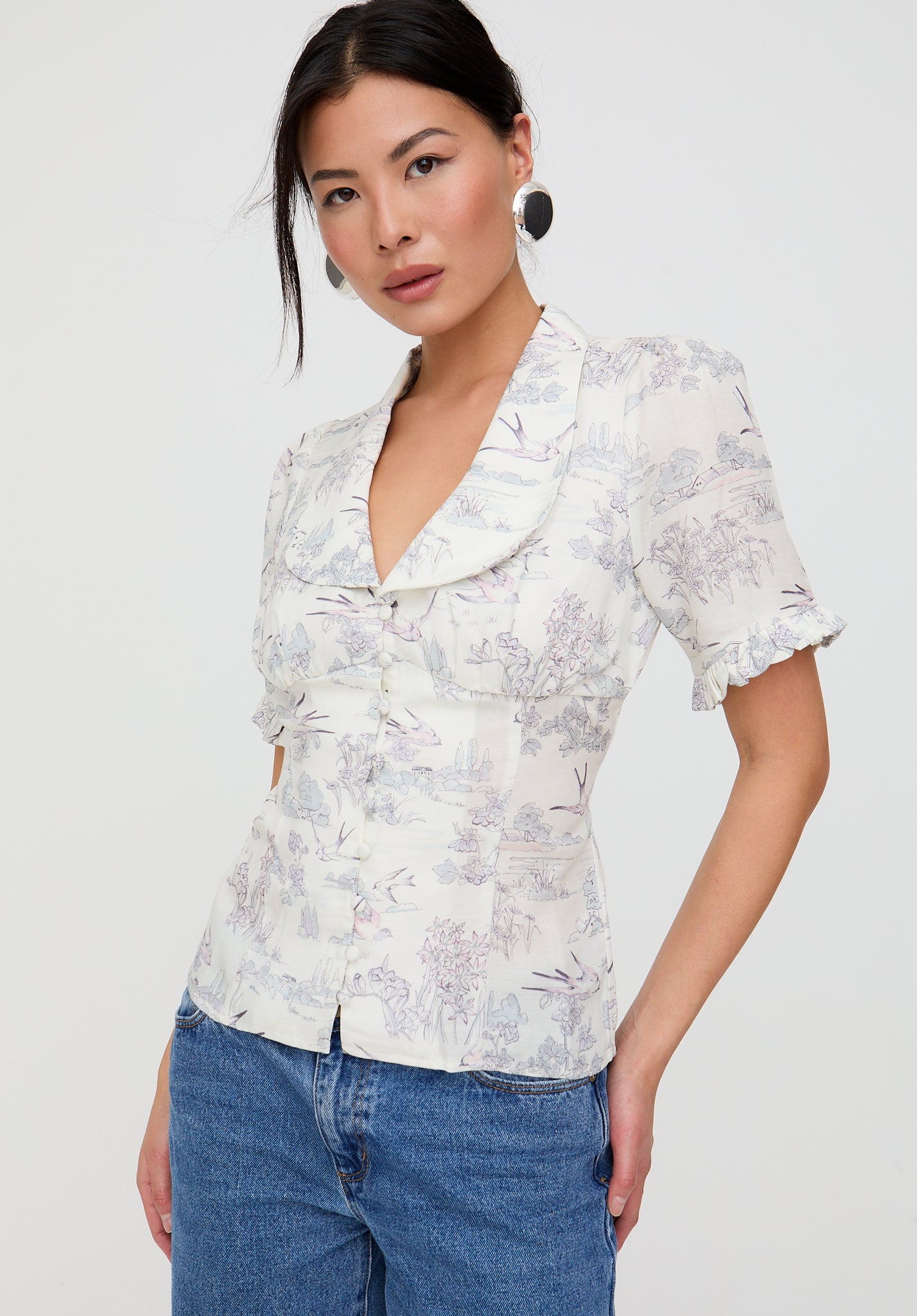 Woman wearing a floral blouse and blue jeans against a white background