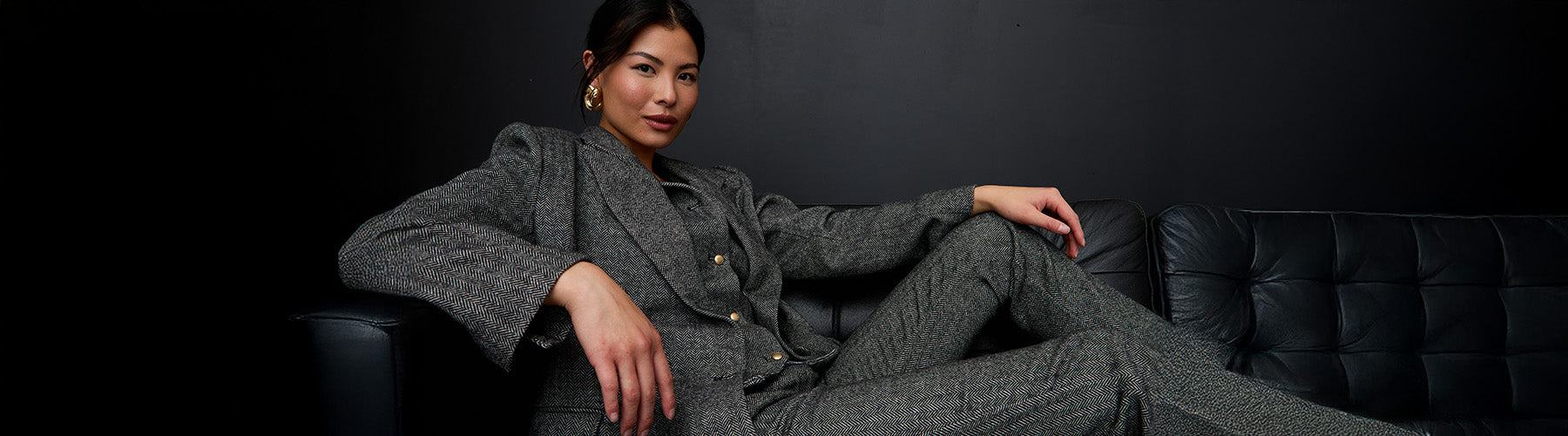 Woman in a gray suit sitting on a black couch against a dark background