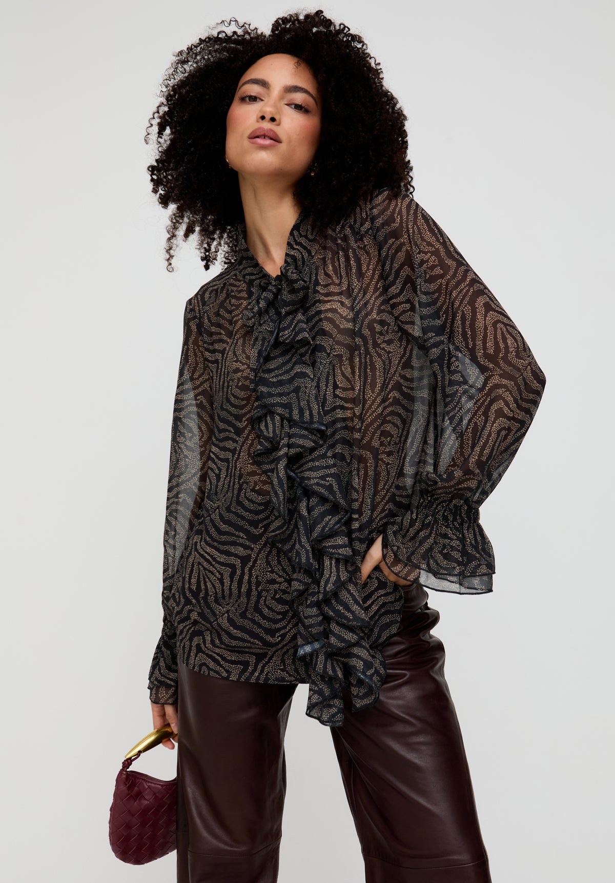 Woman wearing a patterned blouse and leather pants against a plain background