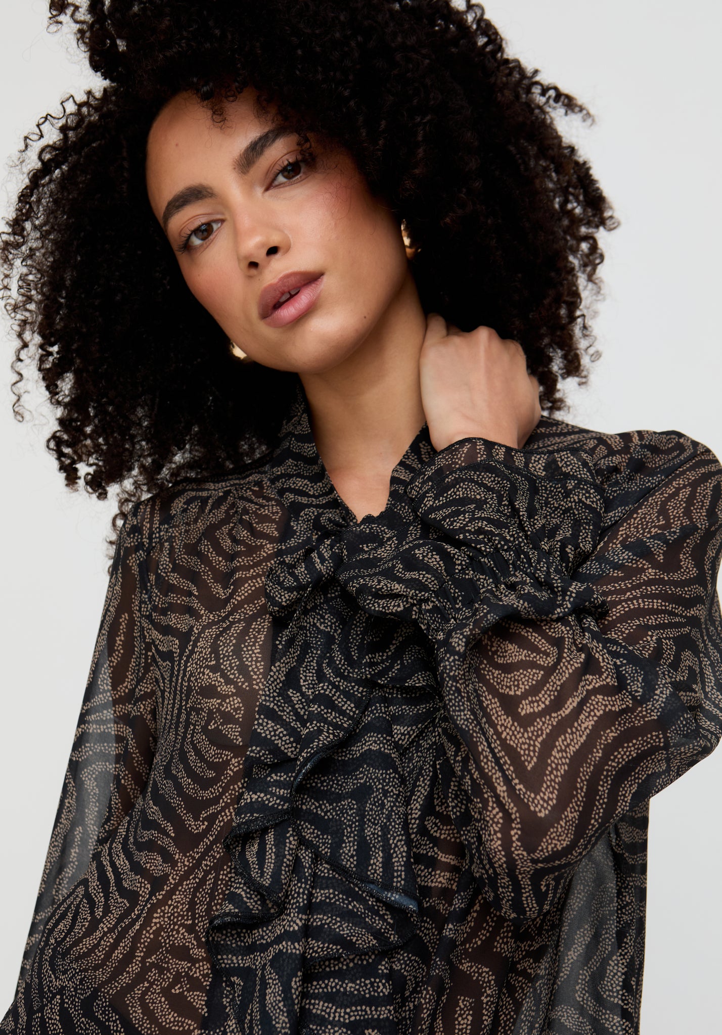 Woman wearing a patterned blouse with a bow detail on a plain background