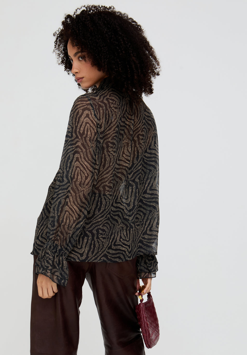 Woman wearing a patterned shirt and holding a red bag against a white background