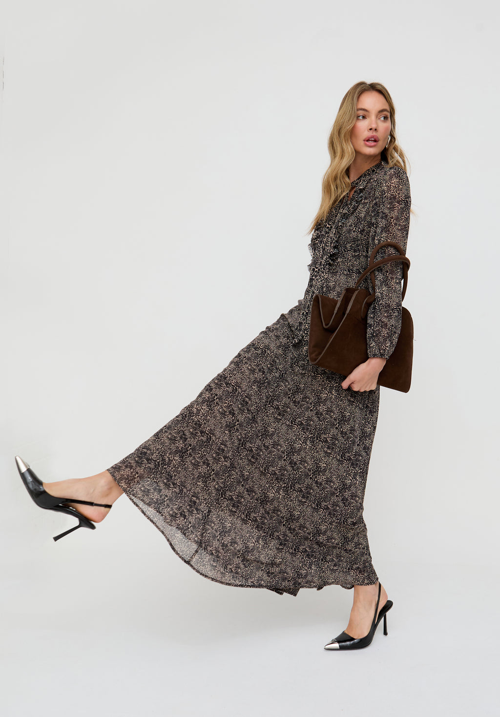 Woman wearing a long floral dress with a brown handbag on a white background