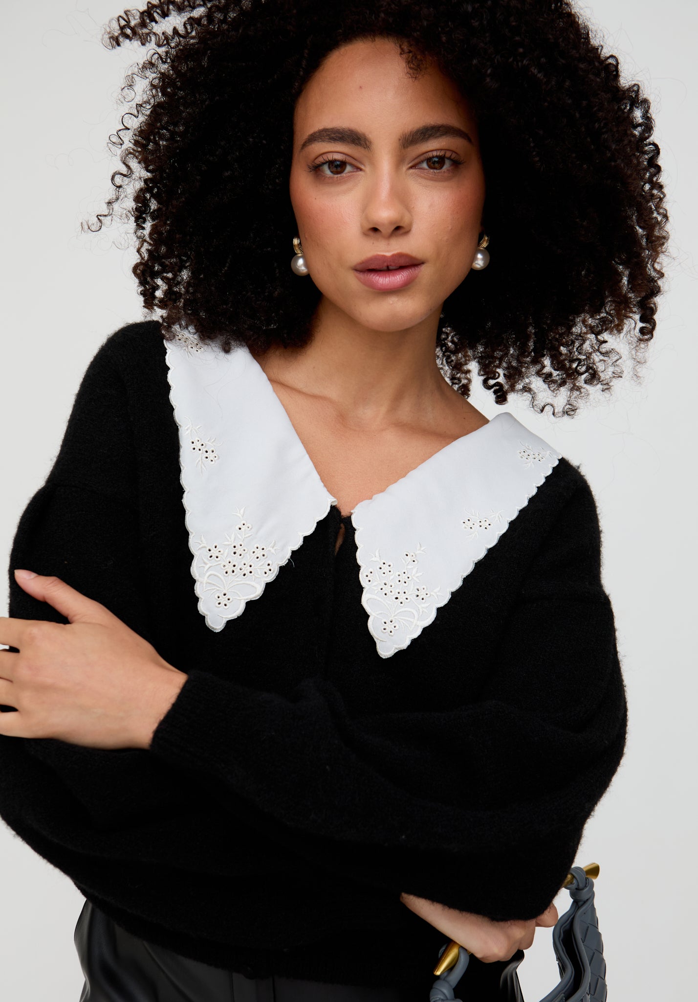 Woman wearing a black sweater with a white collar against a plain background