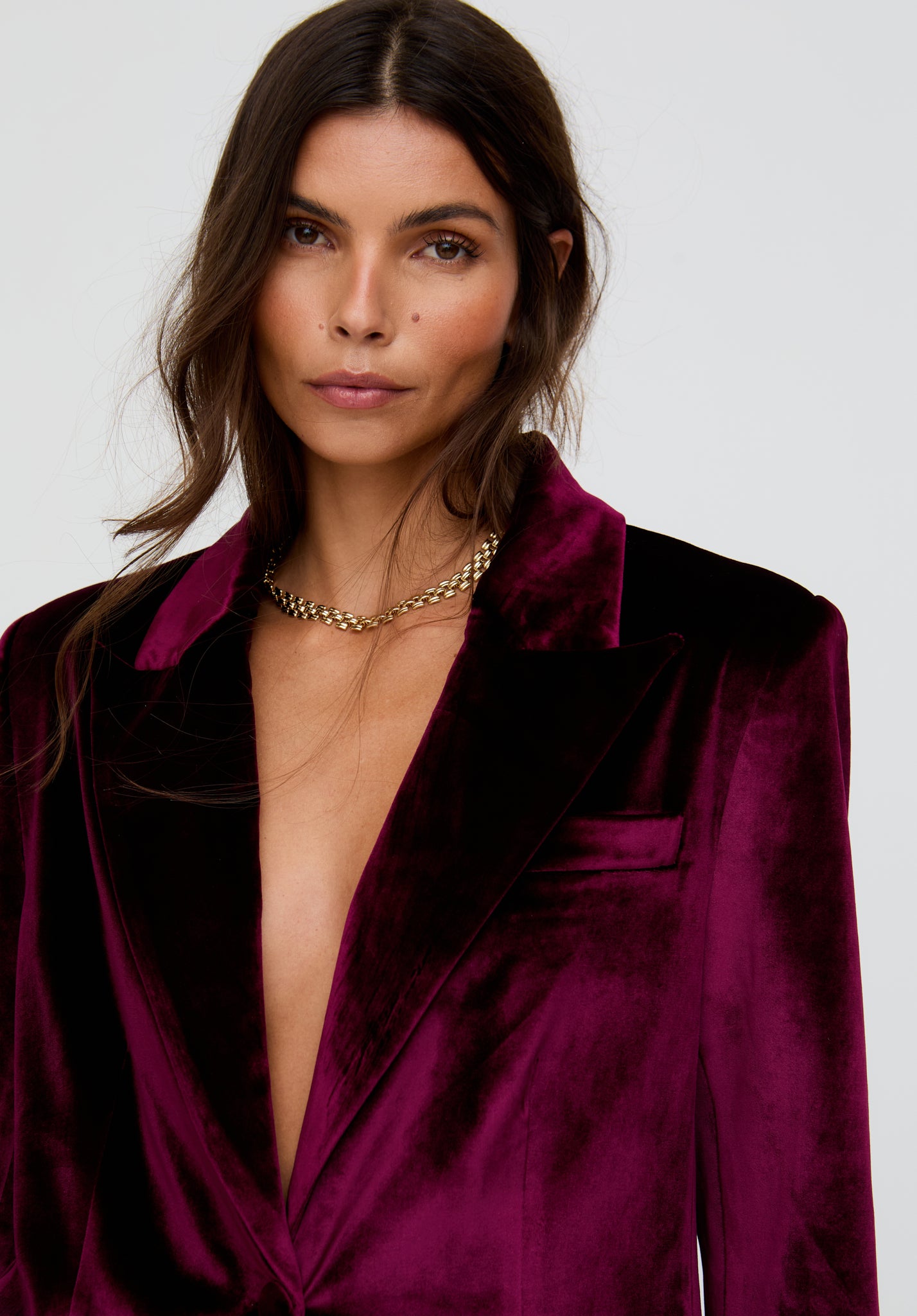 Woman wearing a deep-necked purple satin dress with a gold necklace against a plain background