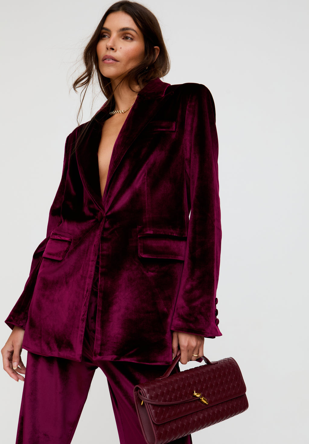 Woman wearing a burgundy velvet suit holding a matching handbag on a white background