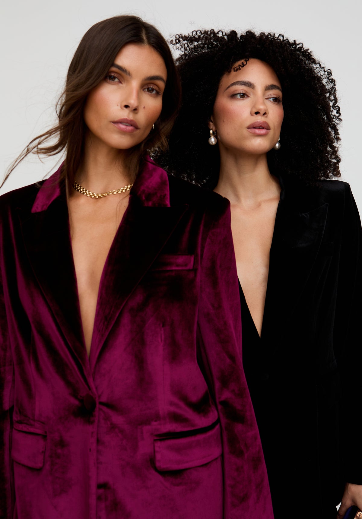Two women wearing deep purple and black velvet suits against a neutral background