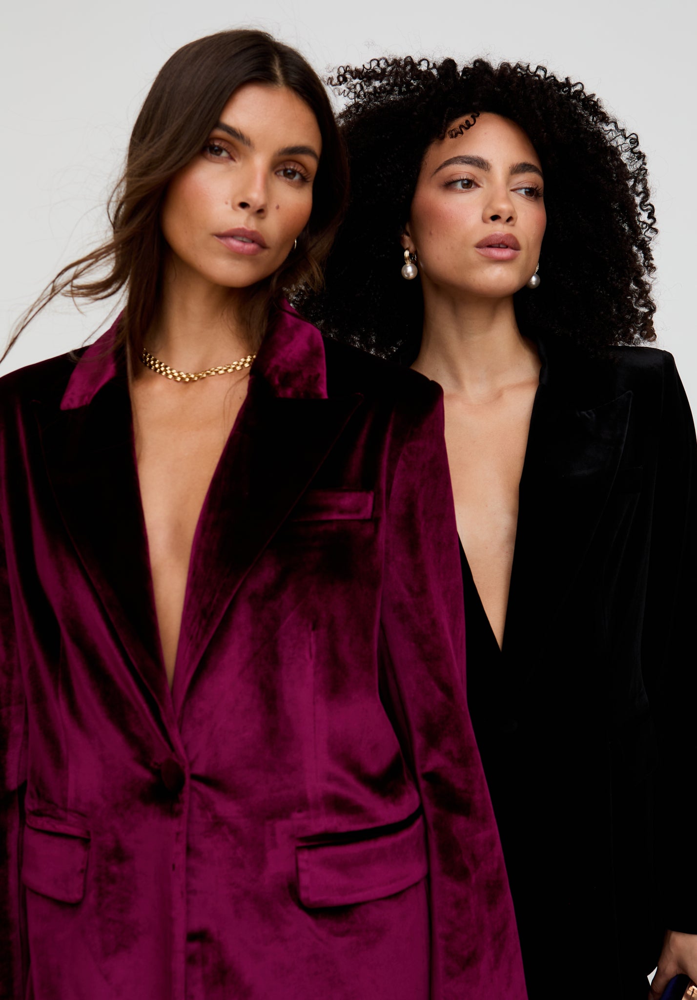 Two women wearing deep purple and black velvet suits against a neutral background
