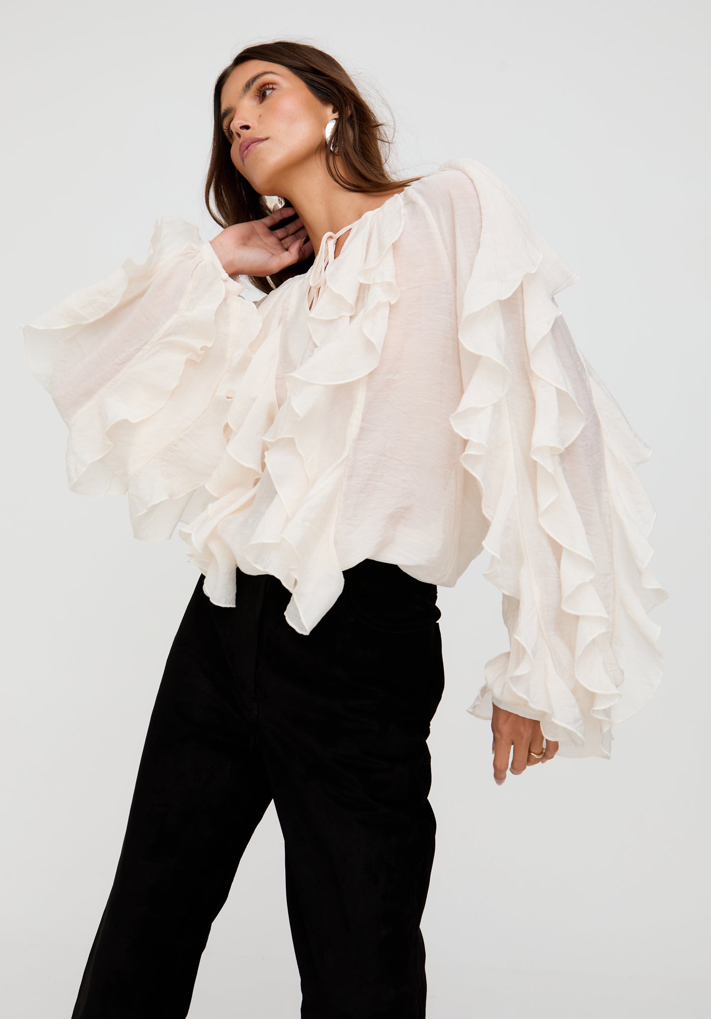 Woman wearing a white ruffled blouse and black pants on a white background