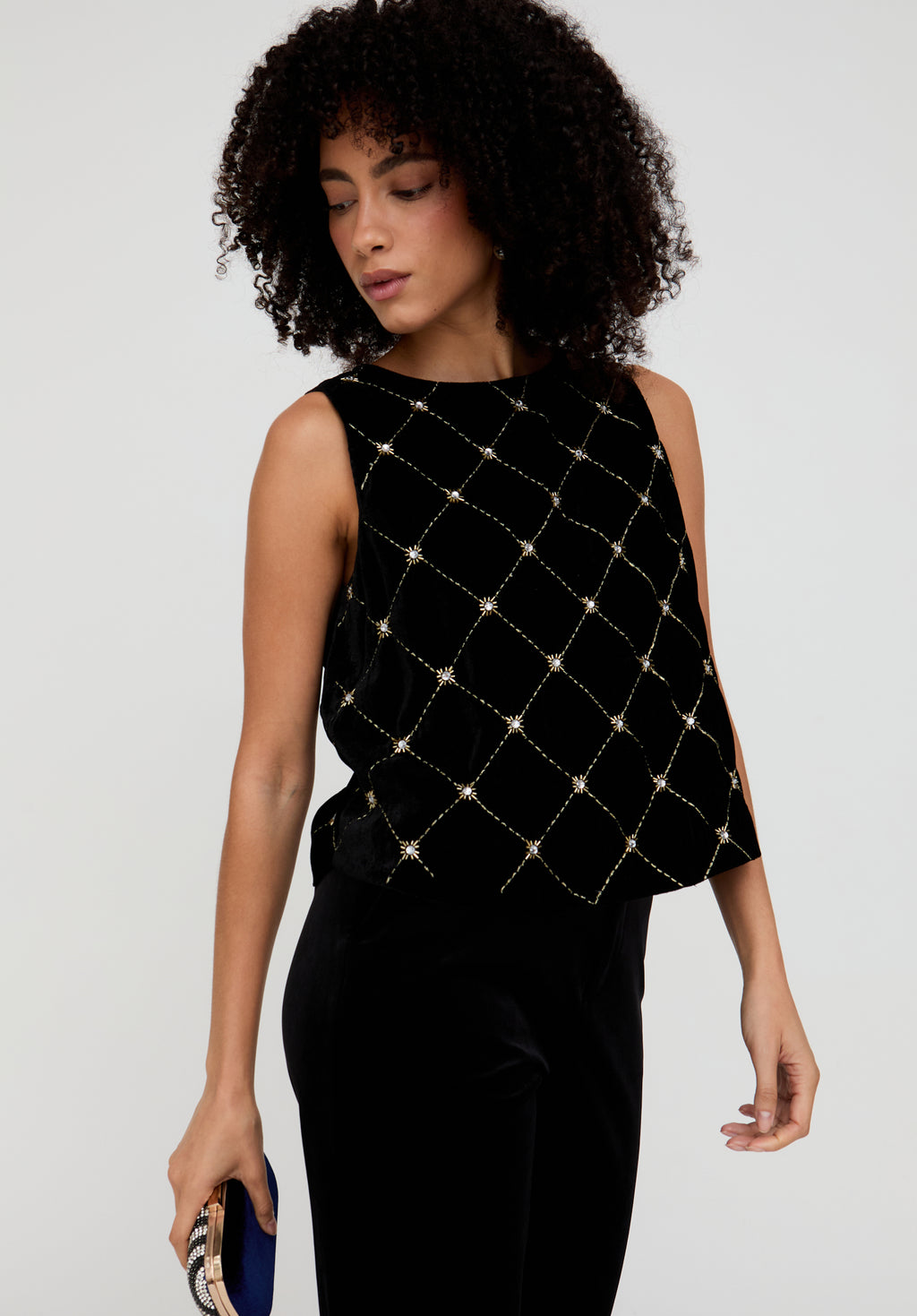 Woman wearing a black sleeveless top with gold embellishments on a plain background
