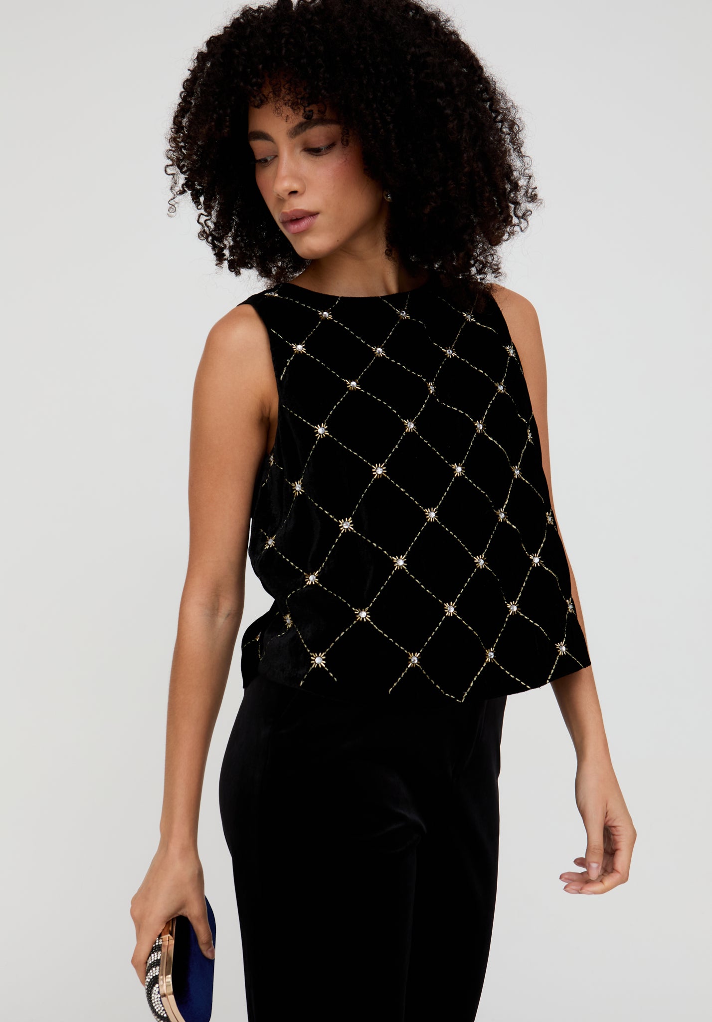 Woman wearing a black sleeveless top with gold embellishments on a plain background