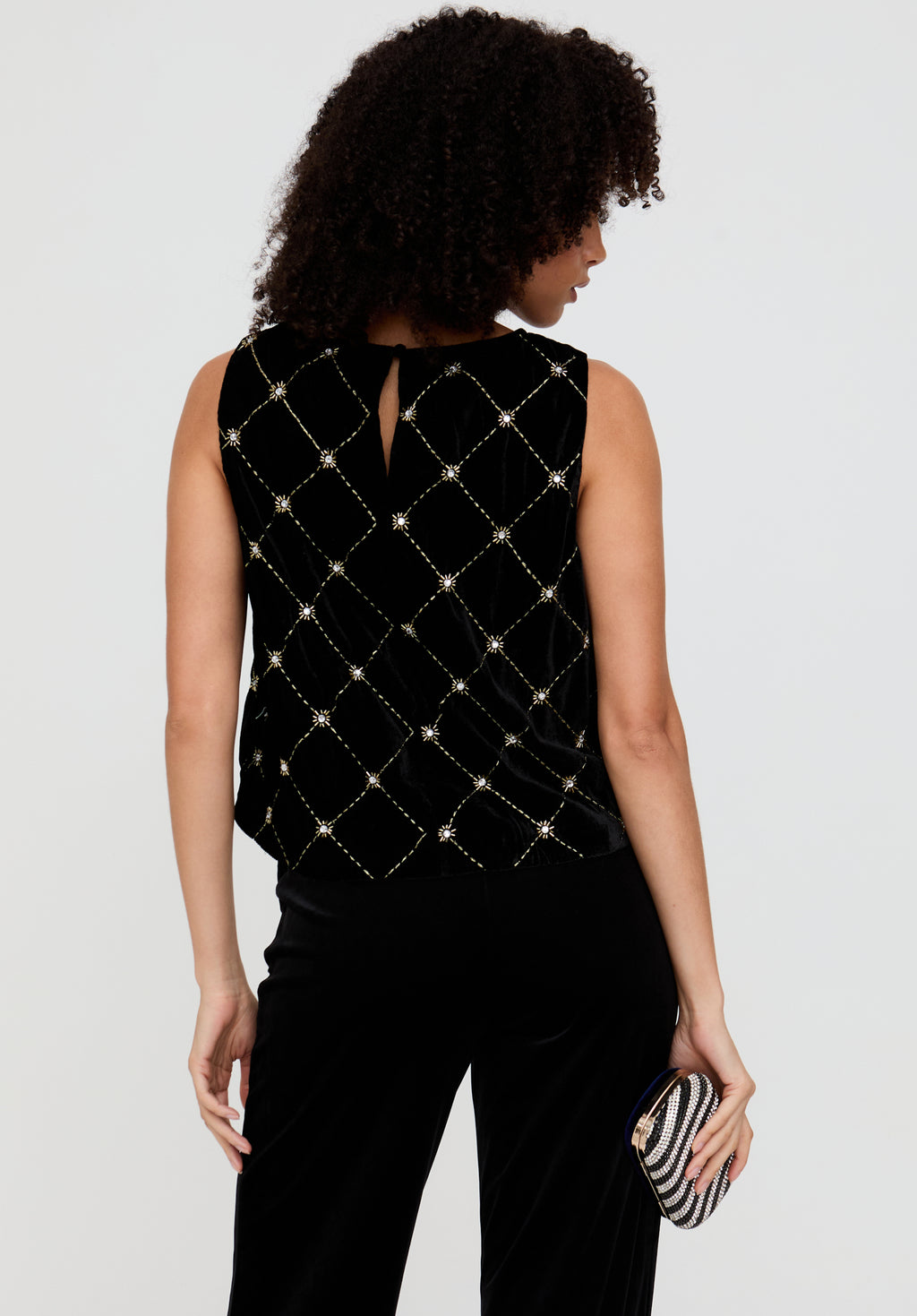 Woman wearing a black sleeveless top with diamond pattern and black pants, holding a striped clutch.
