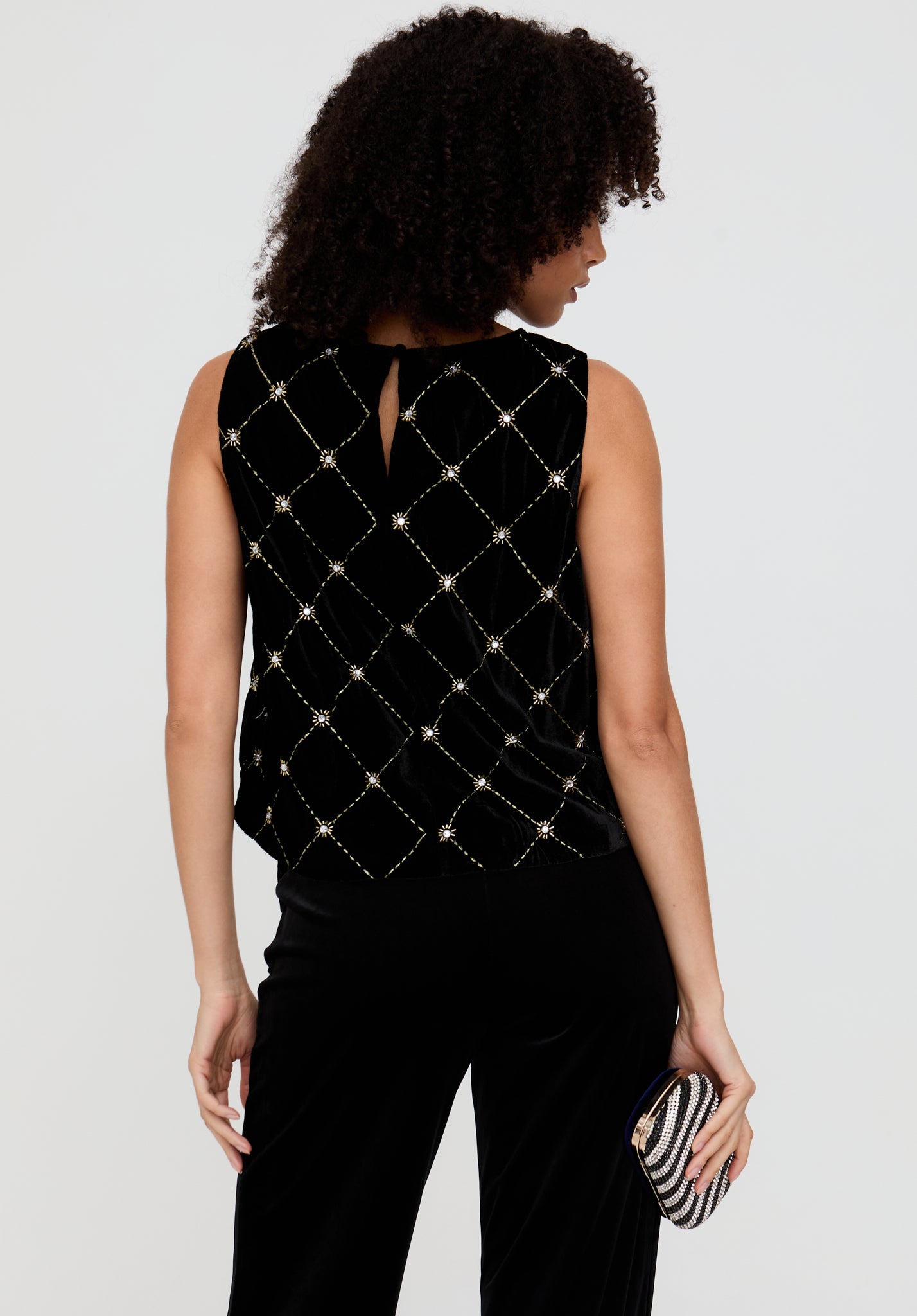 Woman wearing a black sleeveless top with diamond pattern and black pants, holding a striped clutch.