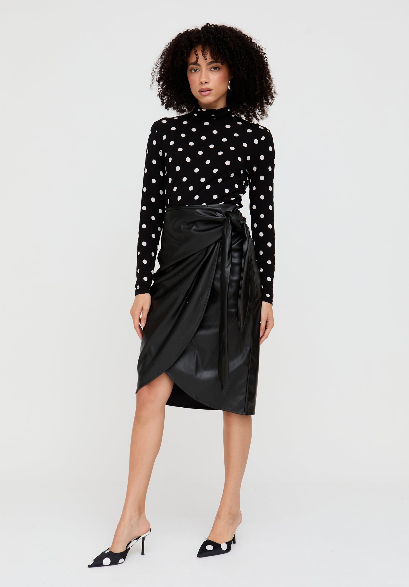 Woman wearing a black polka dot top and black leather skirt on a white background