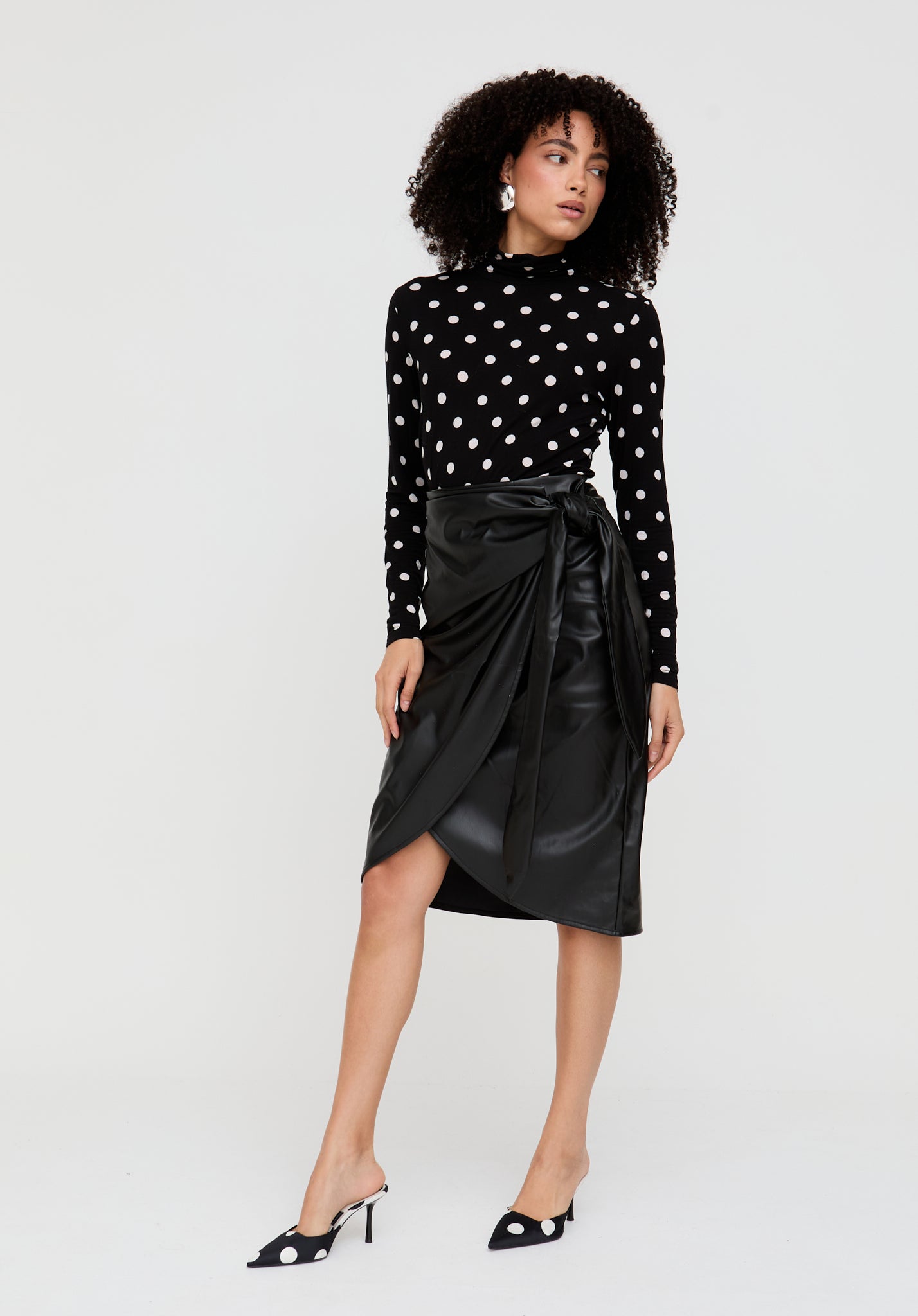 Woman wearing a black polka dot top and black leather skirt on a white background