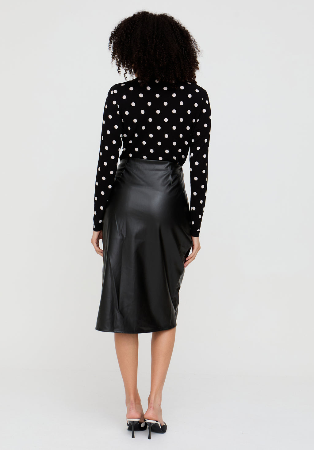 Person wearing a black polka dot blouse and black satin skirt on a white background