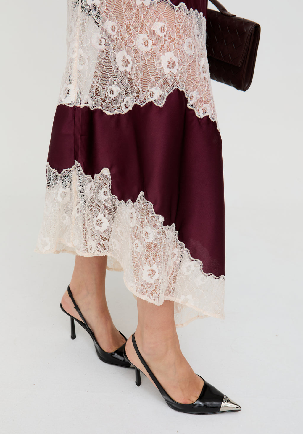 Person wearing a burgundy dress with white lace details and black high-heeled shoes on a light gray background