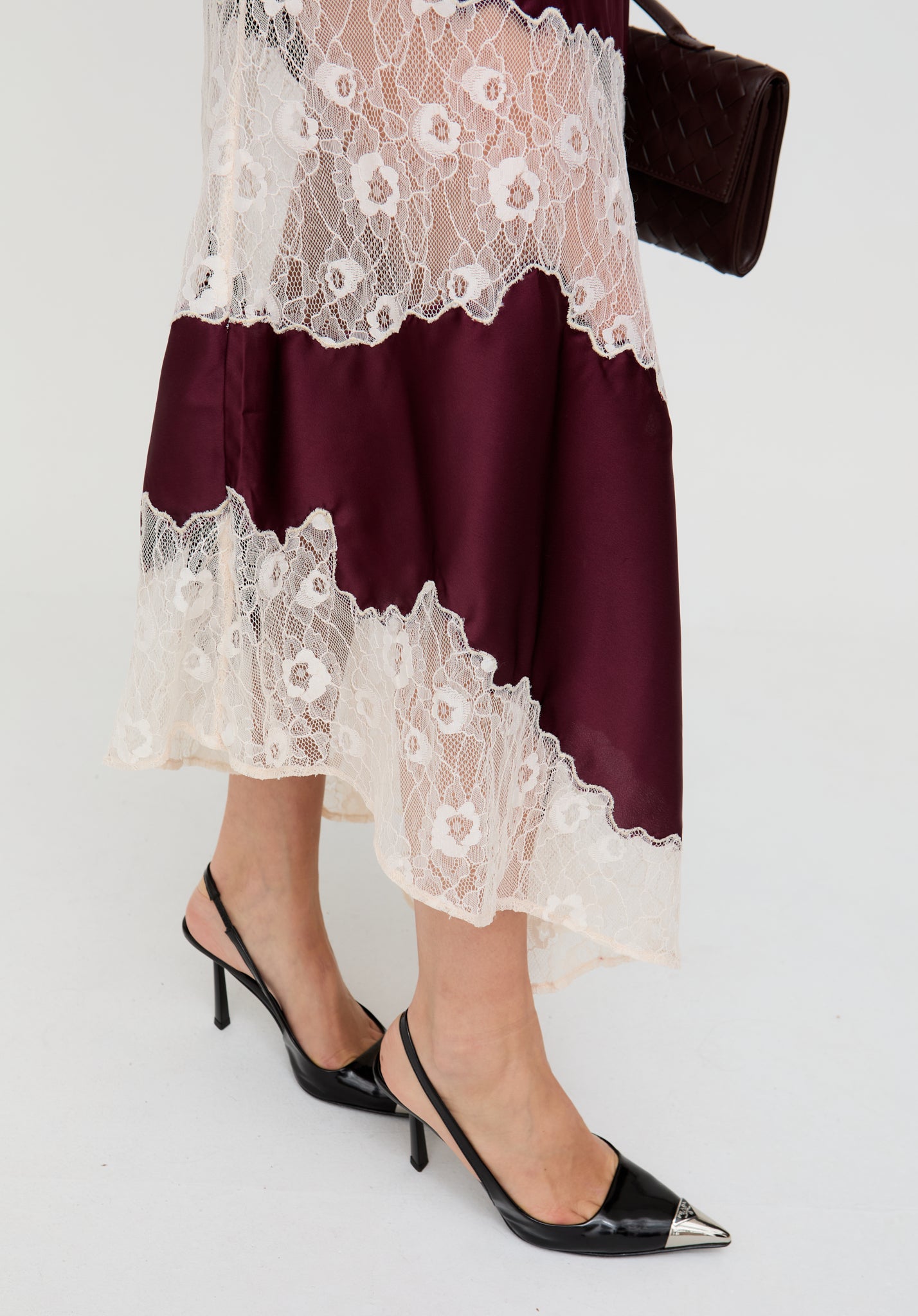 Person wearing a burgundy dress with white lace details and black high-heeled shoes on a light gray background