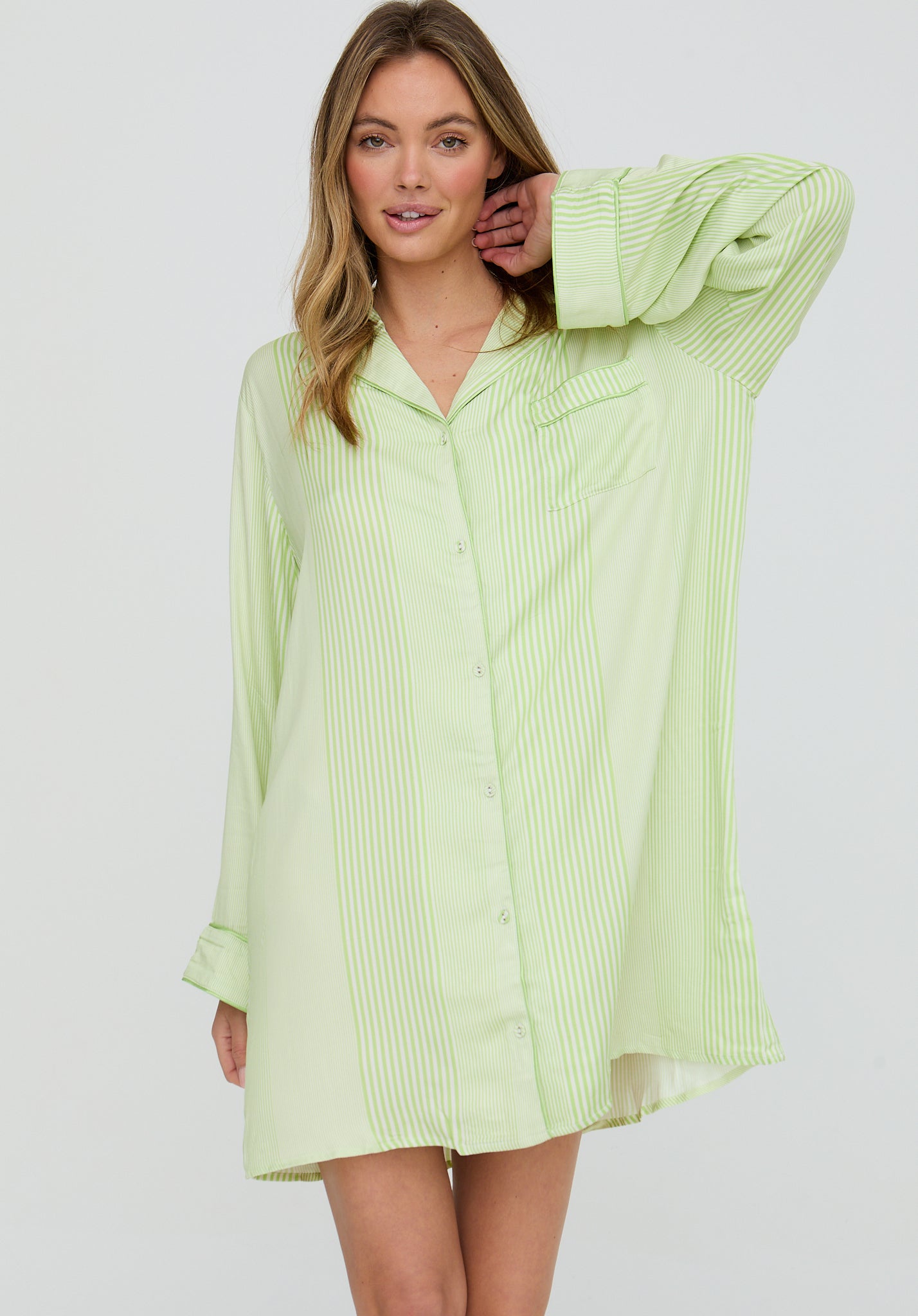 Woman wearing a light green button-up shirt dress on a white background