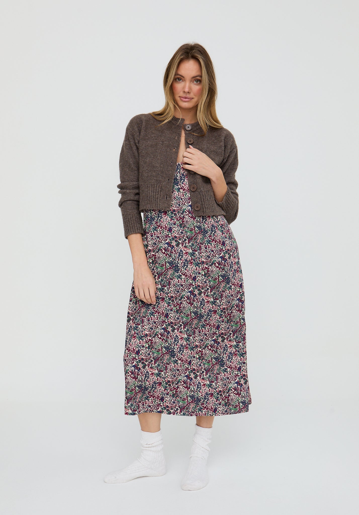 Woman wearing a floral dress and brown cardigan on a white background