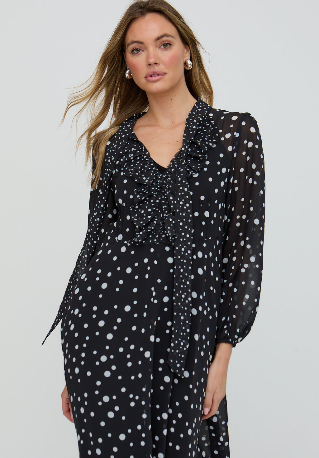 Woman wearing a black dress with white polka dots on a plain background