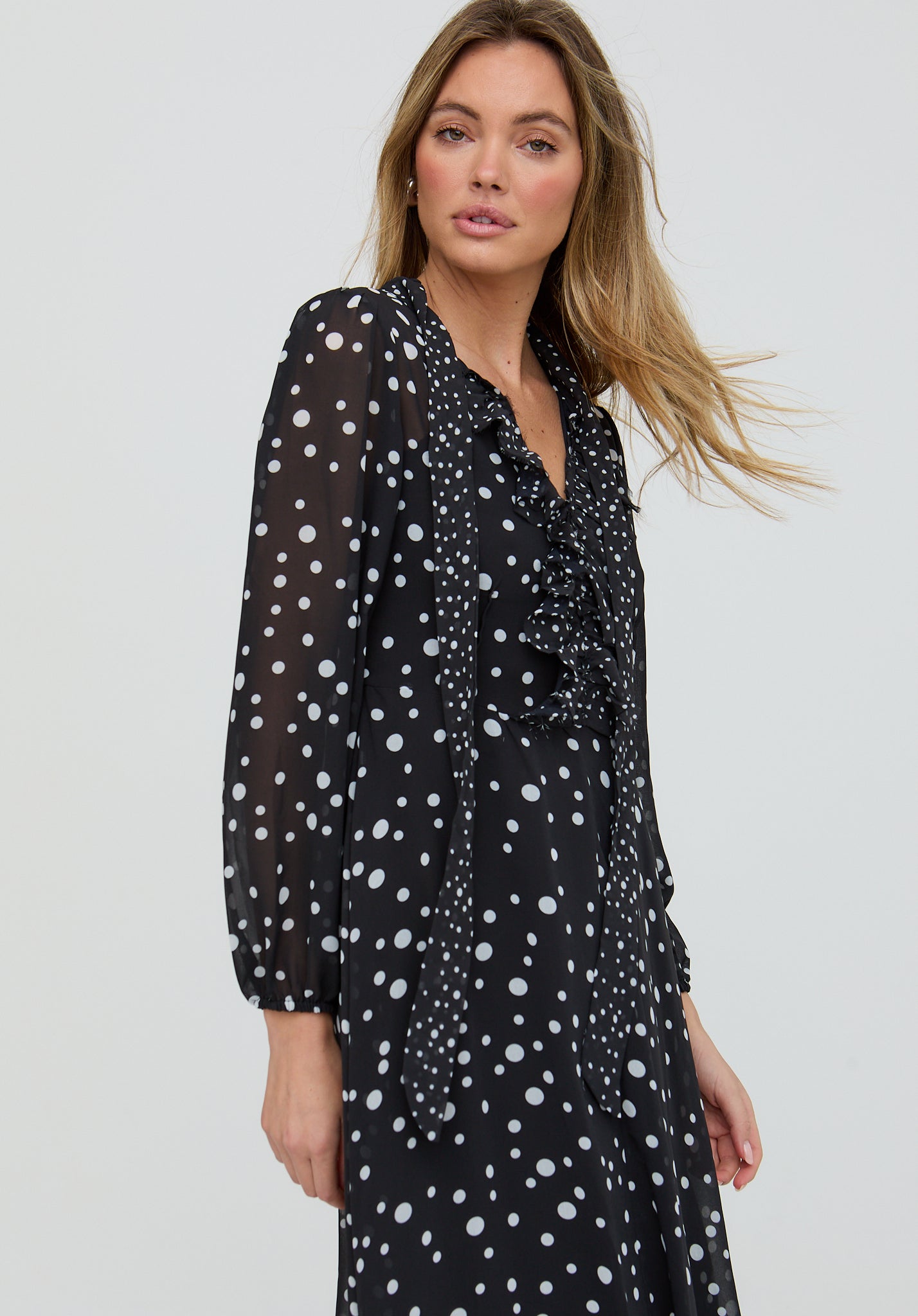 Woman wearing a black dress with white polka dots against a plain background