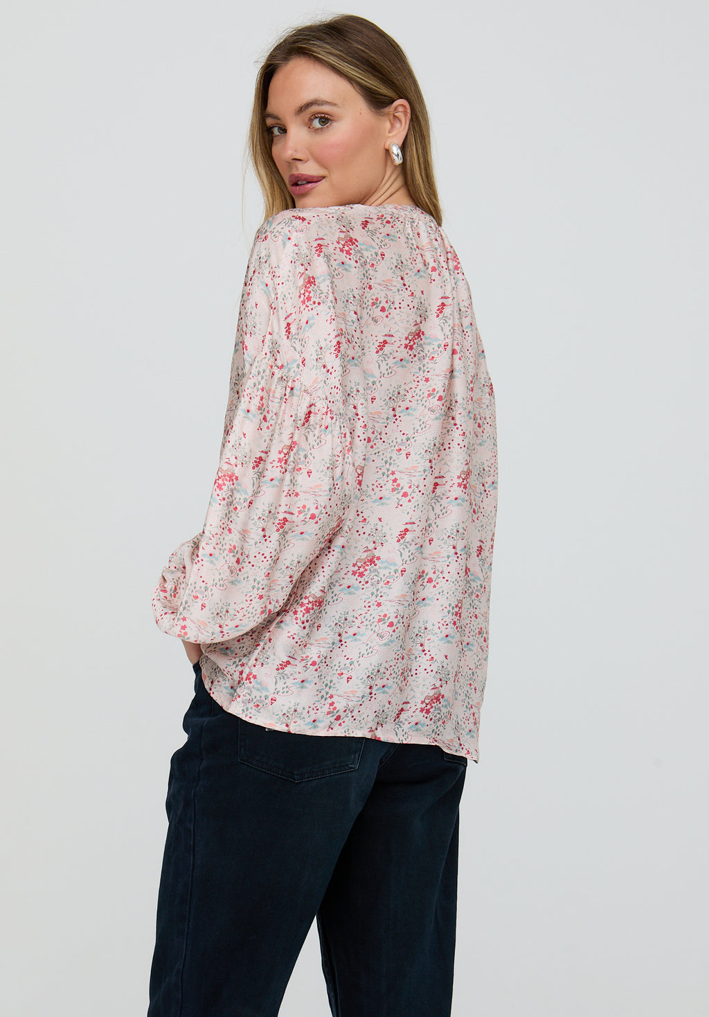 Woman wearing a floral blouse and dark pants on a plain background