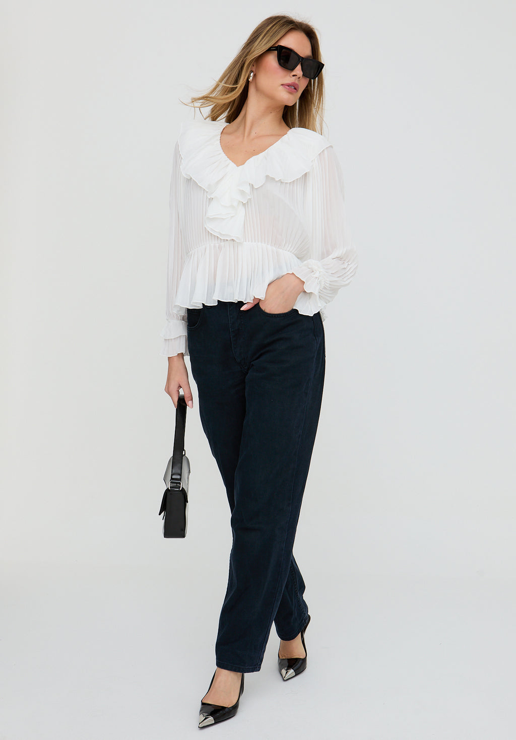 Woman wearing a white blouse and dark pants against a white background