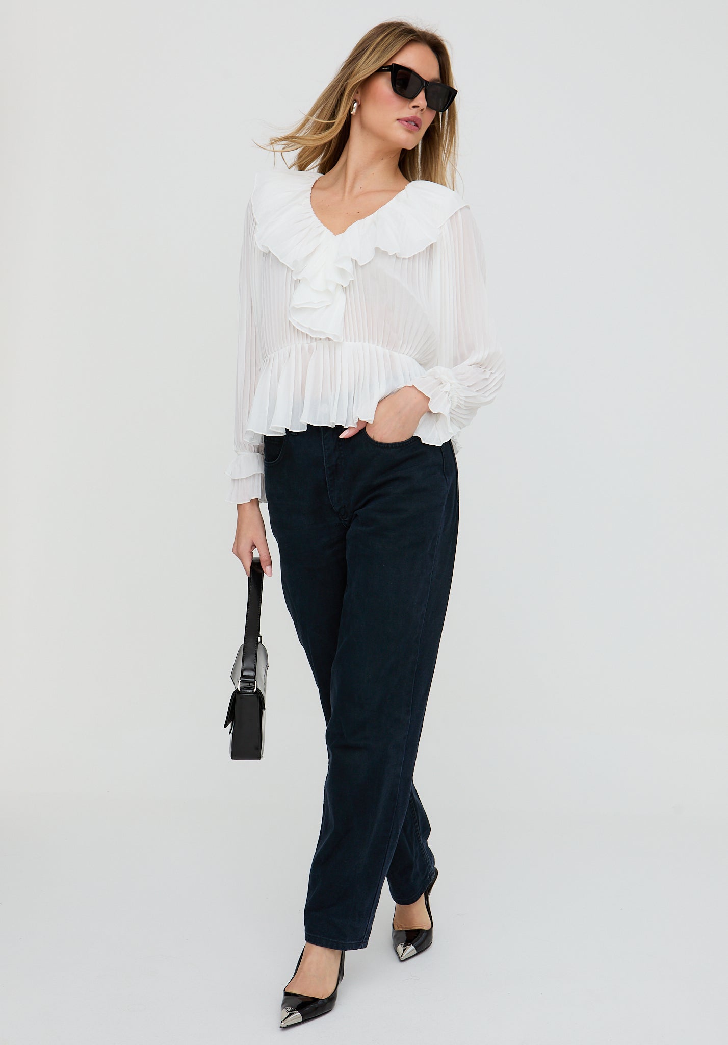 Woman wearing a white blouse and dark pants against a white background