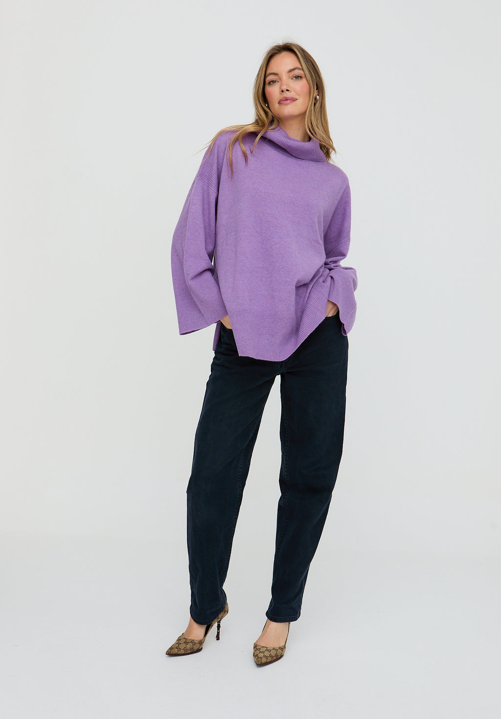 Woman wearing a purple sweater and black pants on a white background