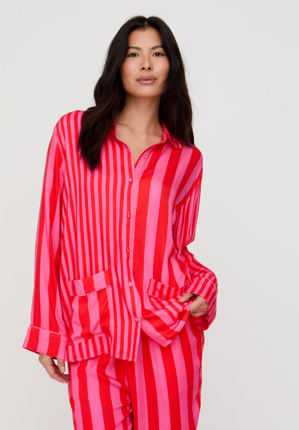 Woman wearing a red and pink striped pajama set against a plain background