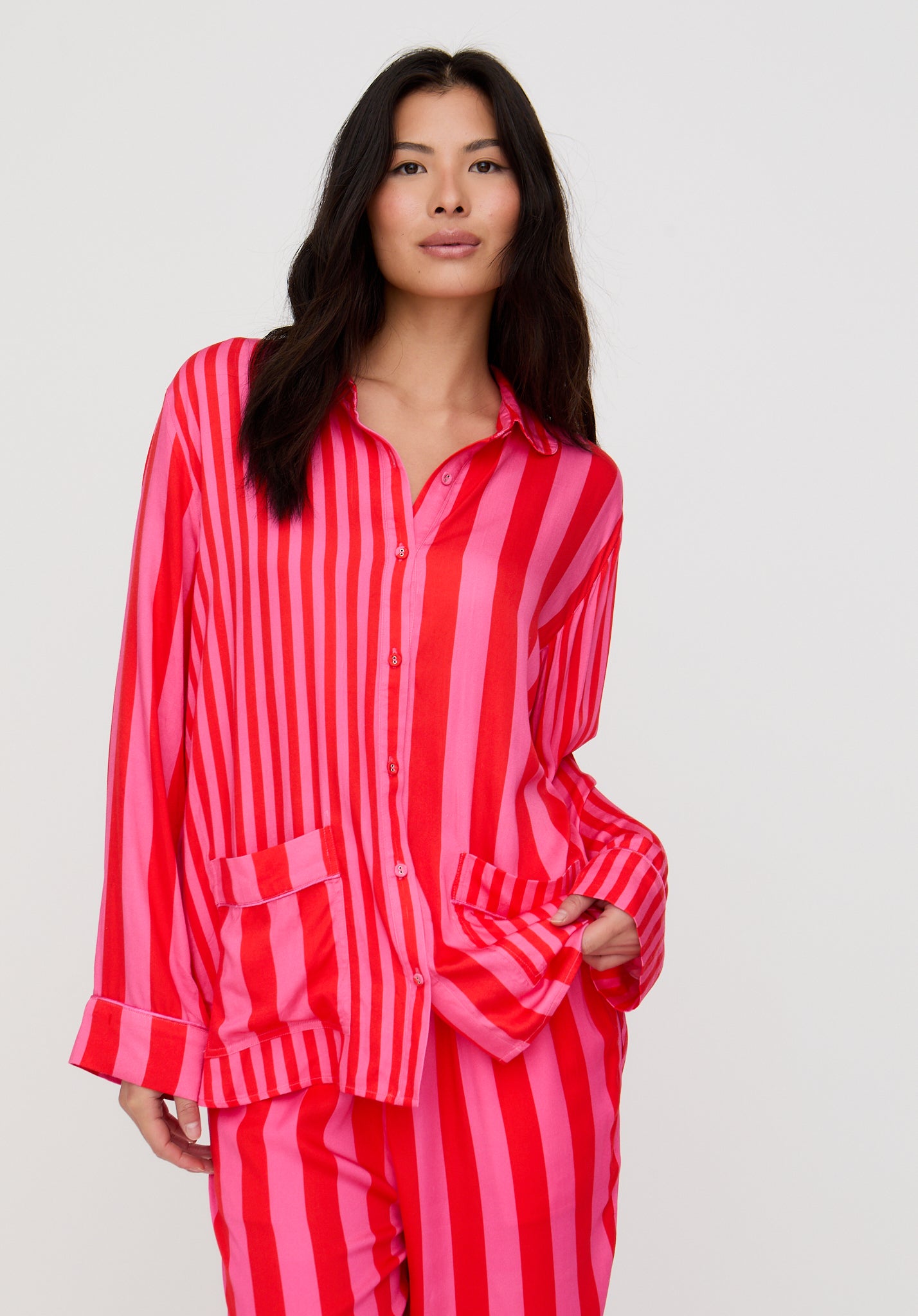 Woman wearing a red and pink striped pajama set against a plain background
