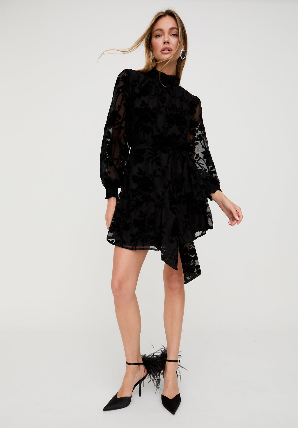 Woman wearing a black lace dress with sheer sleeves on a white background