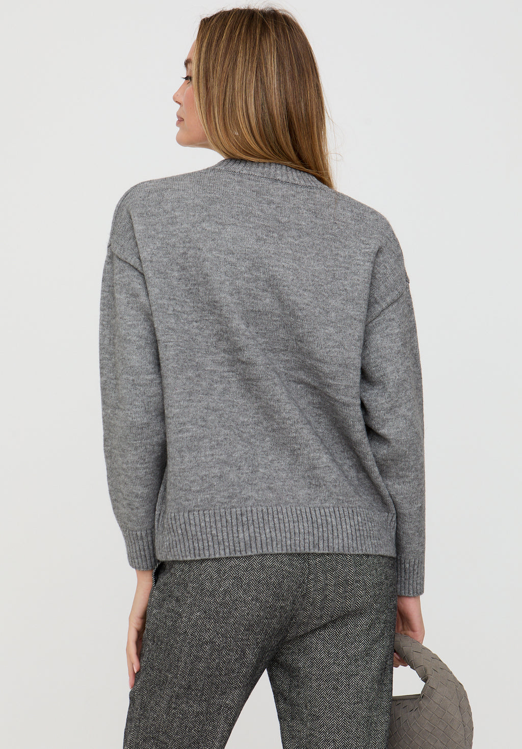 Woman wearing a gray sweater and pants against a white background
