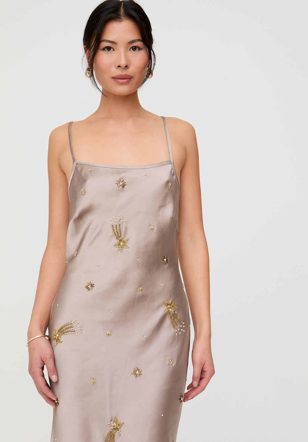 Woman wearing a beige slip dress with gold embroidery on a white background