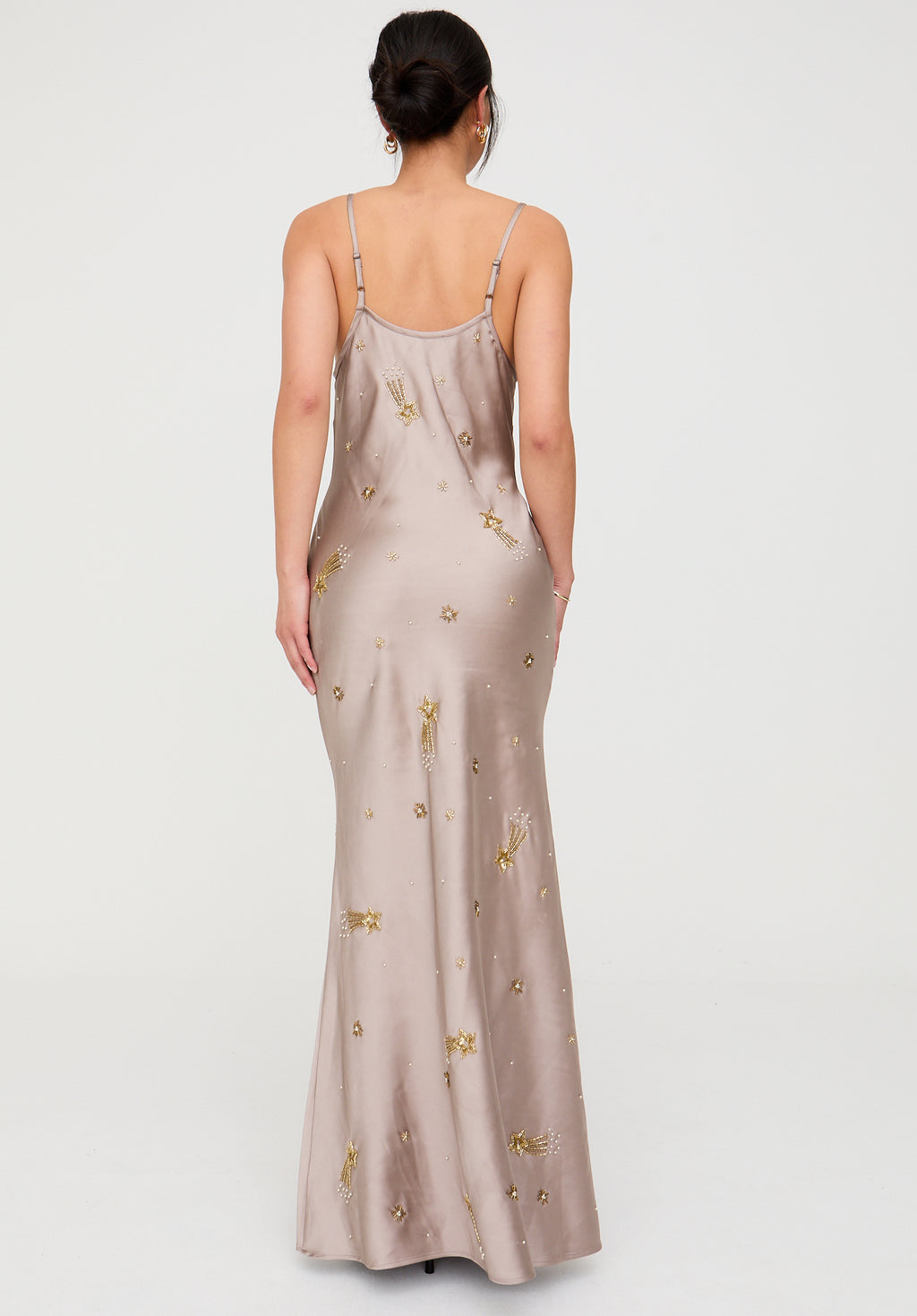 Woman wearing a beige slip dress with gold embellishments on a white background