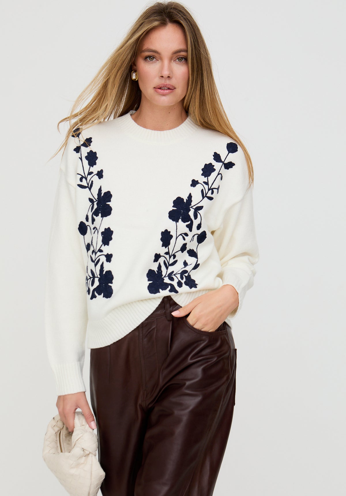 Woman wearing a white sweater with black floral patterns on a plain background