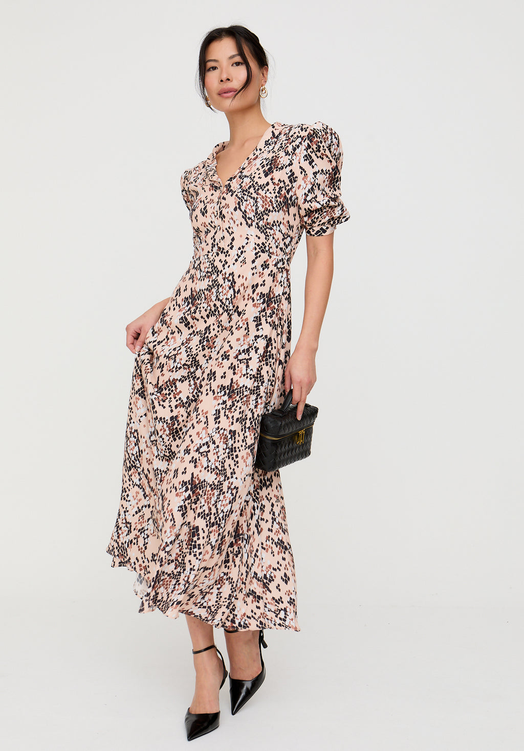Woman wearing a floral dress holding a clutch against a white background